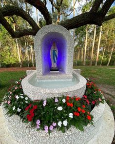 there is a statue in the middle of some flowers and plants around it with purple light coming from behind