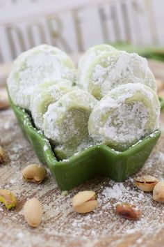 powdered sugar balls in a green bowl on a wooden board with nuts and pistachios