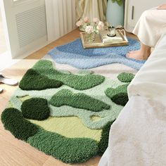 a person sitting on a bed in front of a rug with green and blue shapes