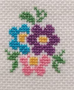 a close up of a cross stitch pattern on a white cloth with colorful flowers in the center