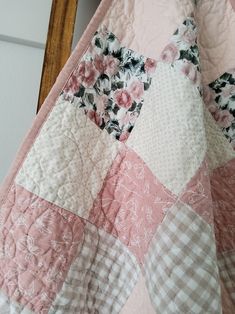 a pink and white quilt hanging from a wooden chair next to a wall with flowers on it