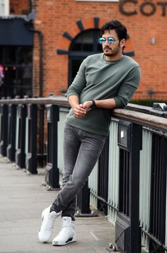 a man leaning on a fence with his arms crossed, wearing sunglasses and looking at the camera