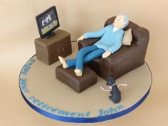 a cake that has a man laying on a chair with a cat and tv in the background