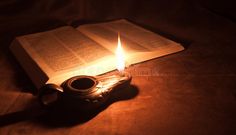 an open book sitting on top of a table with a lit candle next to it