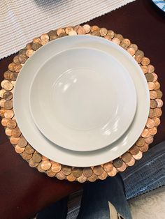 two white plates with gold coins on them sitting on top of a wooden table next to a person's legs