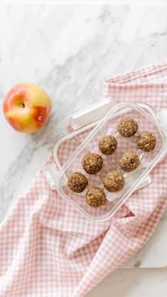 an apple and some food in a plastic container on a white marble counter top next to a red checkered napkin