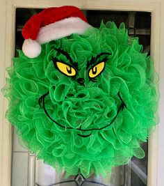 a green wreath with yellow eyes and a santa's hat on it is hanging from the front door