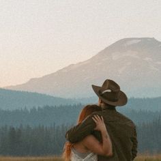 a man and woman embracing each other in front of a mountain