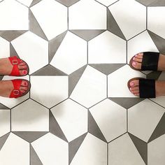 two pairs of feet with red and black toenails standing on a tiled floor