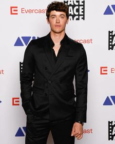 a young man in a black suit posing for a photo on the red carpet at an event