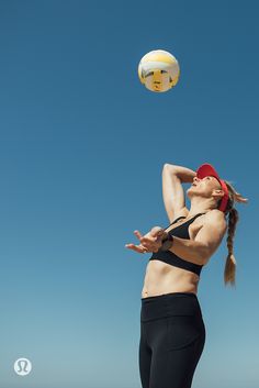 a woman in black shorts and red headband playing with a white ball on the beach