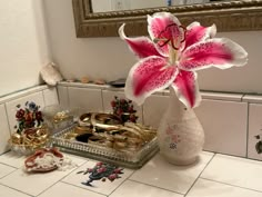 a white vase filled with pink flowers sitting on top of a counter next to jewelry