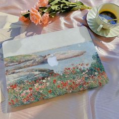 an apple laptop sitting on top of a bed next to flowers and a cup of coffee