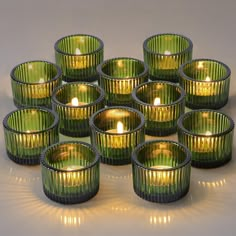 twelve green glass tealight holders with lit candles in the middle on a white surface