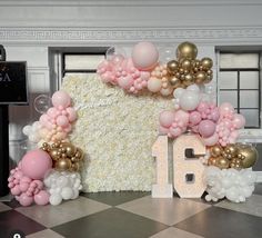 a large number surrounded by balloons and flowers in front of a wall with the number 16 on it