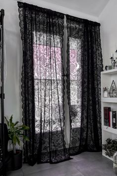 a living room with black curtains and white shelves filled with books, vases and plants