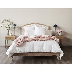 a bed with white linens and pink blankets on it, in a room with wood flooring