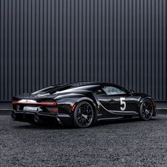 a black sports car parked in front of a metal building with the number 5 on it