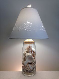 a lamp that is on top of a table with shells in the jar underneath it