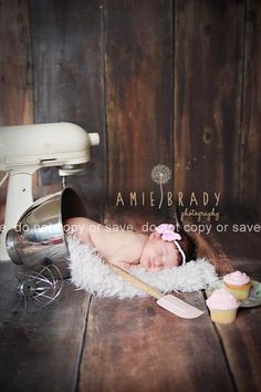 a baby is laying down on the floor next to a mixer and cupcakes