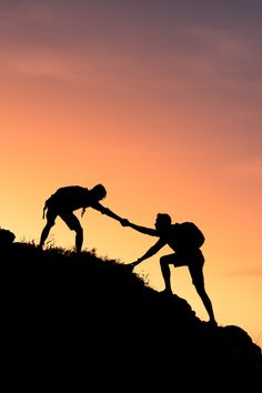 two people are helping each other to climb up a hill with their hands together as the sun sets in the background