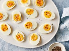 an overhead view of hard boiled eggs on a white plate next to a bowl of seasoning