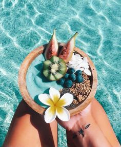 a person's feet in the water holding a bowl with fruit and cereal on it