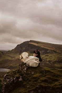 a bride and groom standing on top of a rock in the middle of a mountain