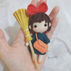 a hand holding a doll with a broom in it's right hand and a small orange bag on the other hand