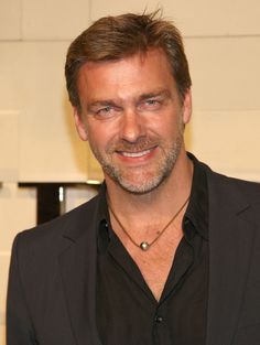 a man in a suit smiling at the camera with his hand on his hip and wearing a black shirt