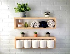 two wooden shelves with towels, plants and toiletries on them against a white brick wall