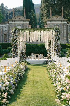 an outdoor wedding ceremony setup with white flowers and greenery on the lawn, surrounded by tall hedges