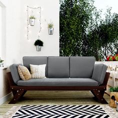 a gray couch sitting on top of a wooden floor next to potted plants and trees