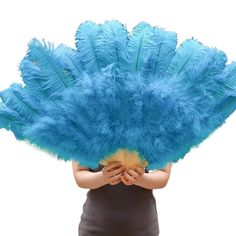 a woman holding a blue feather fan in her hands and covering her face with both hands