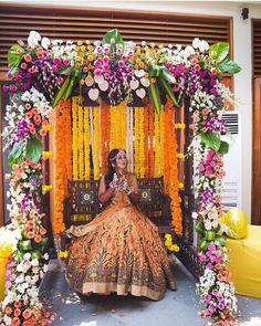 a woman sitting in front of a flower covered stage with flowers on it's sides