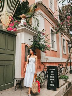 a woman standing in front of a building with flowers on the roof and holding a handbag