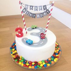 a birthday cake with cars and candy on the top is decorated in white frosting