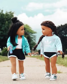 two dolls standing next to each other on a road with trees and grass in the background