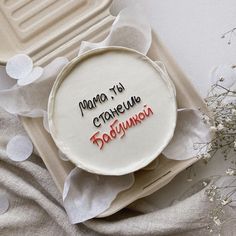 a cake with writing on it sitting on top of a tray next to flowers and paper