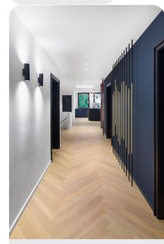 an empty hallway with wooden floors and black doors on either side of the corridor is lit by recessed lights