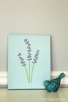 a blue bird sitting on top of a table next to a purple flower painted on the wall