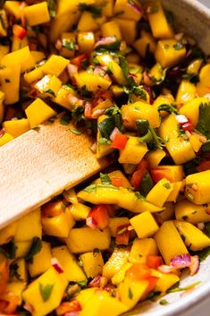 a wooden spoon in a bowl filled with mango salsa