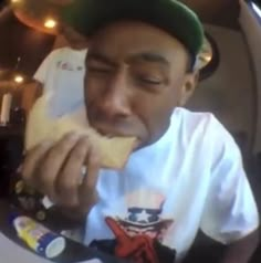 a man sitting in a car eating food from his hand while wearing a green hat