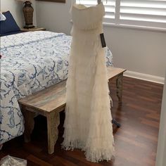 a white dress hanging on a clothes rack in a bedroom next to a wooden bench