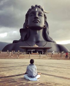 a person sitting on the ground in front of a large buddha statue with its eyes closed