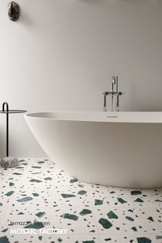 a white bath tub sitting on top of a tiled floor next to a wall mounted faucet