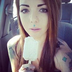 a woman with piercings is holding an ice cream bar in her hand and looking at the camera