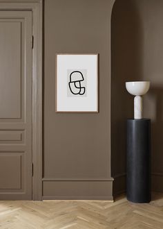 a black and white vase sitting in front of a wall with a framed print on it