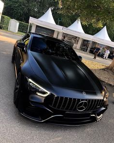 a black mercedes is parked on the side of the road in front of some tents