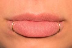 a woman's lips with pink lipstick on the bottom and silver ring around her lip